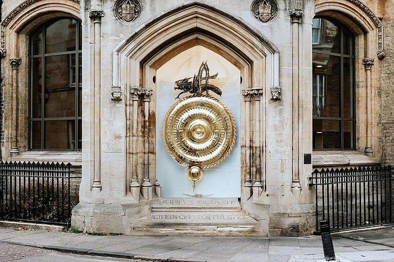 Intricate golden sundial on historic Cambridge building facade, part of guided tours.