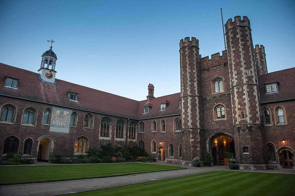 Historic Cambridge college building during twilight with lush green lawn and tower.