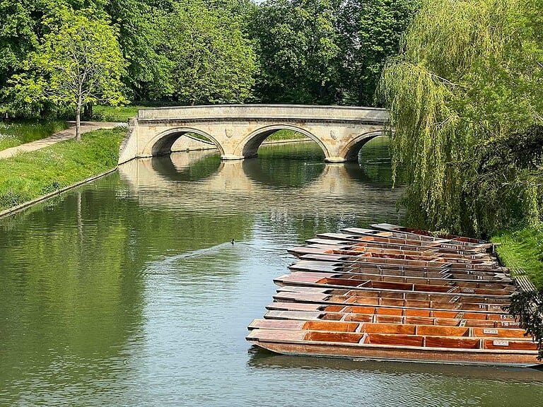 Serene Cambridge river with historic stone bridge and boat rentals, perfect for sightseeing tours.