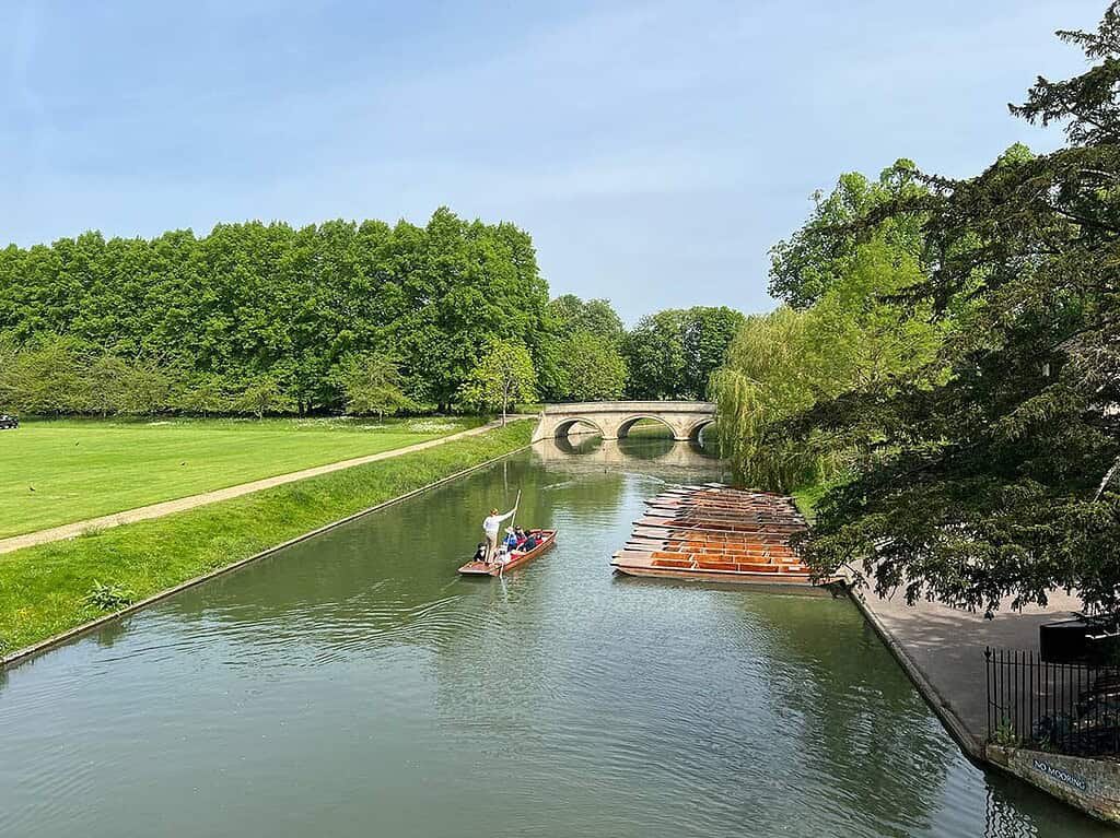 Queens' Green and River Cam in Cambridge with paddle boat, historic bridge, lush trees, and perfect scenery.